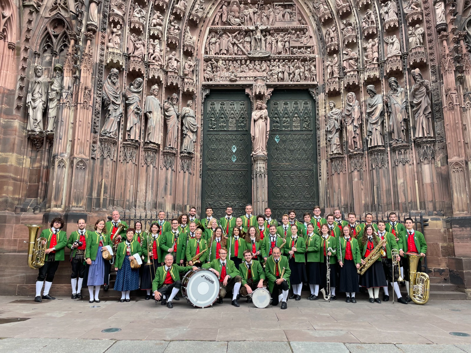 Gesamte Musikkapelle steht in voller Tracht aufgereiht vor dem Dom in Straßburg